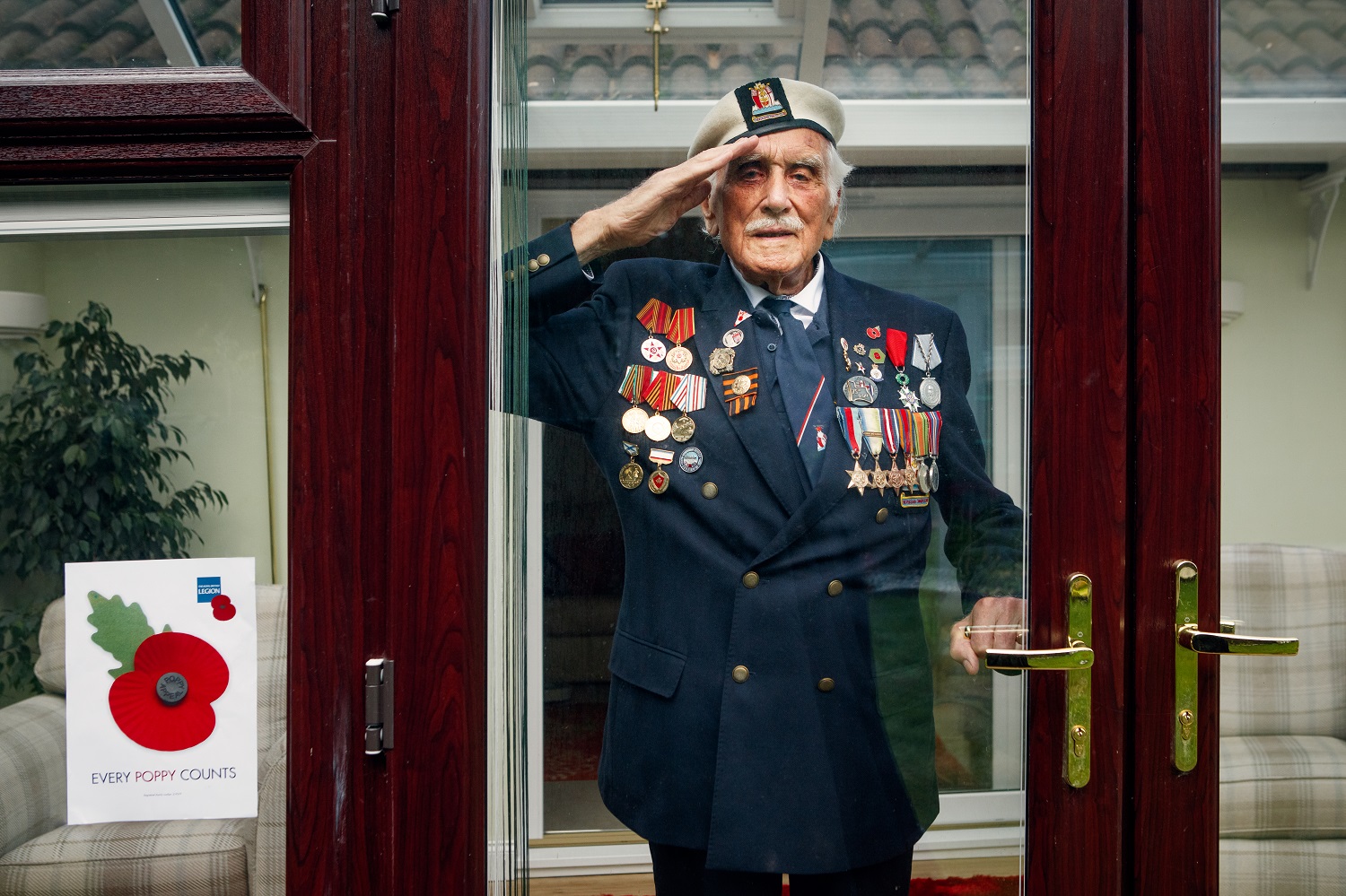 Bill Taylor saluting behind a window wearing his medals